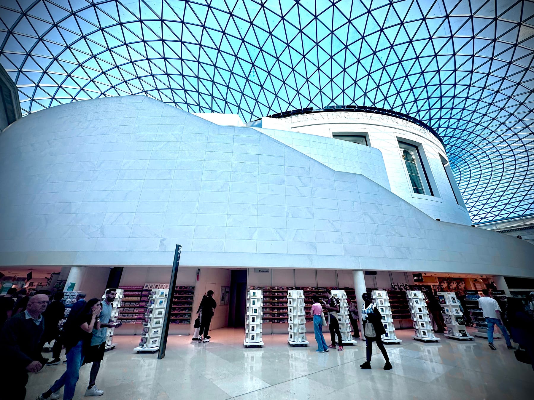 A great glass-roofed courtyard, its lattice canopy curving overhead above a pale stone rotunda, small figures below.