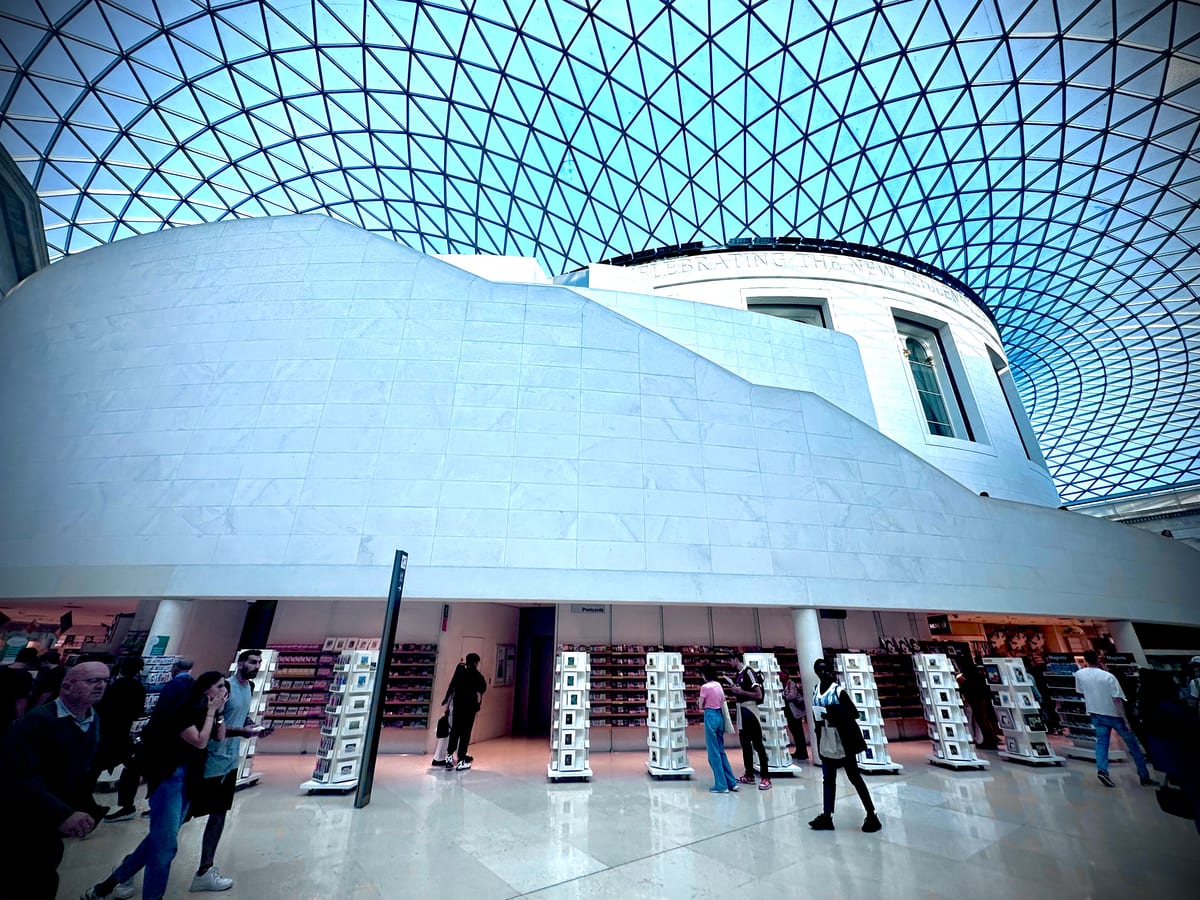 A great glass-roofed courtyard, its lattice canopy curving overhead above a pale stone rotunda, small figures below.