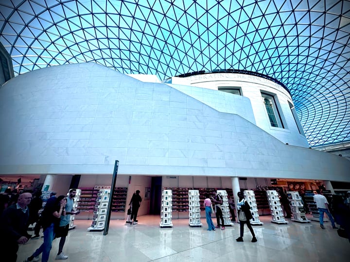 A great glass-roofed courtyard, its lattice canopy curving overhead above a pale stone rotunda, small figures below.