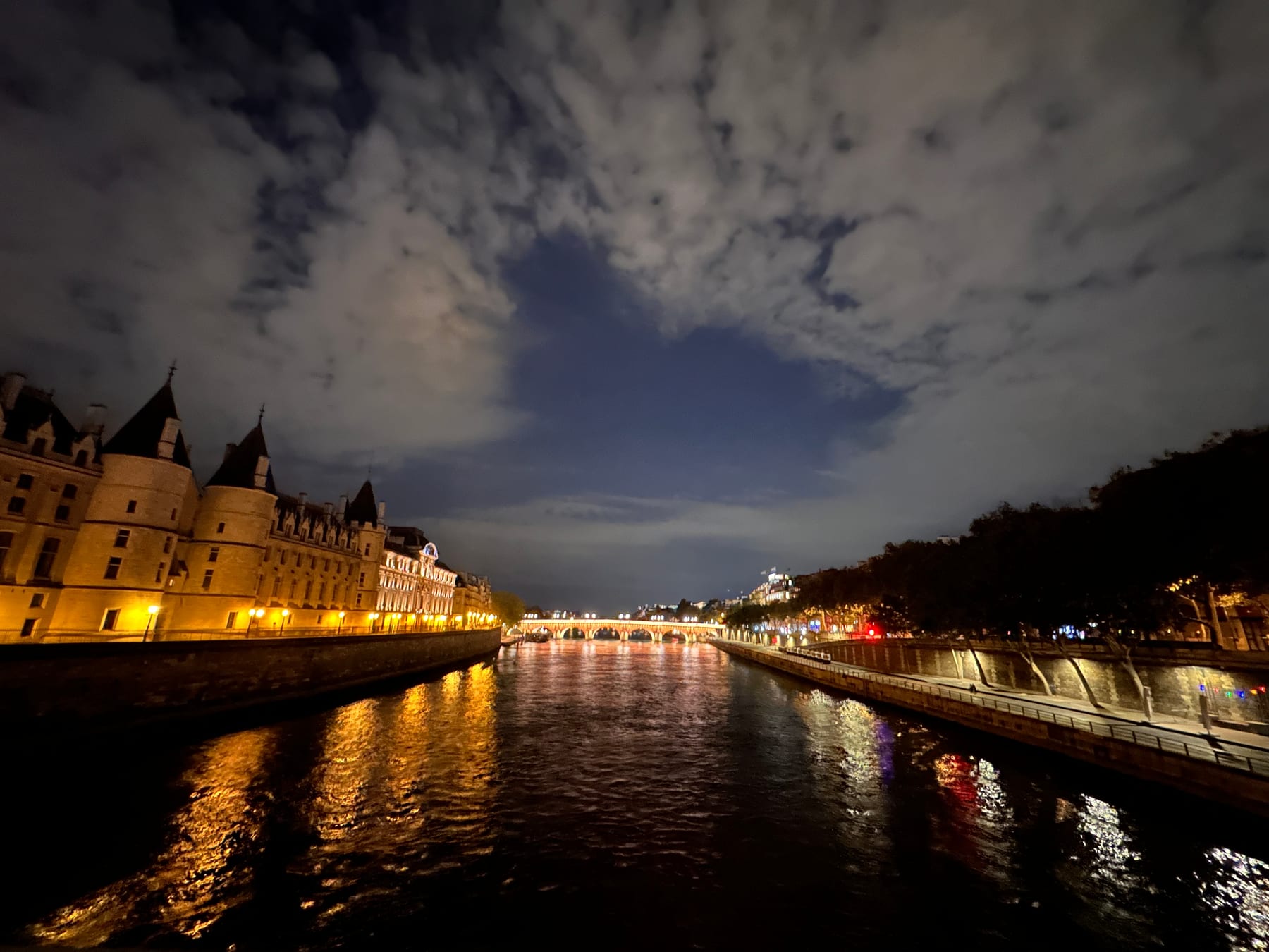 A river at night threading between lit embankments and bridges, golden reflections trembling on the dark water.