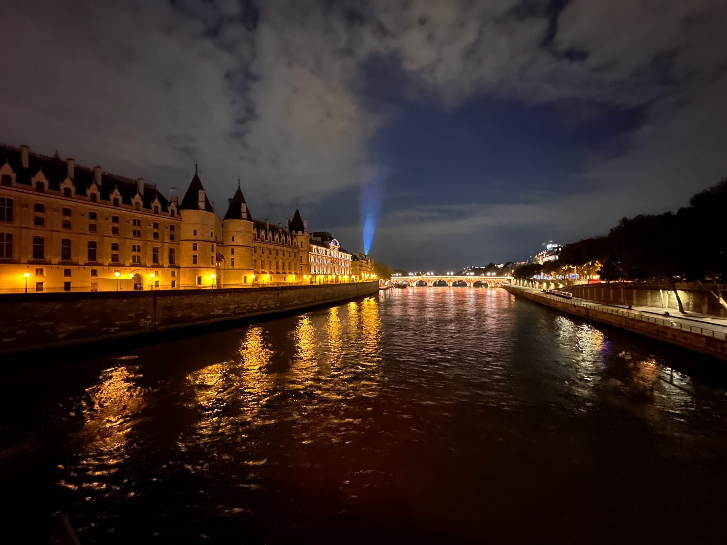 A grand riverside building glowing gold at night, its light spilling across the still water.