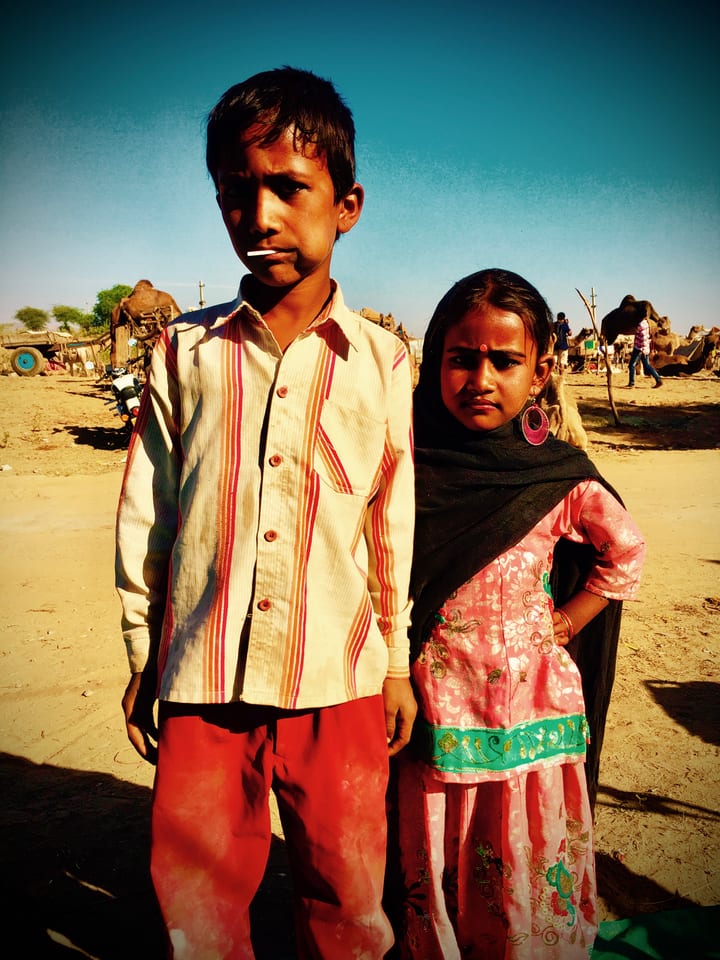 Two children stand together before a distant desert fort.