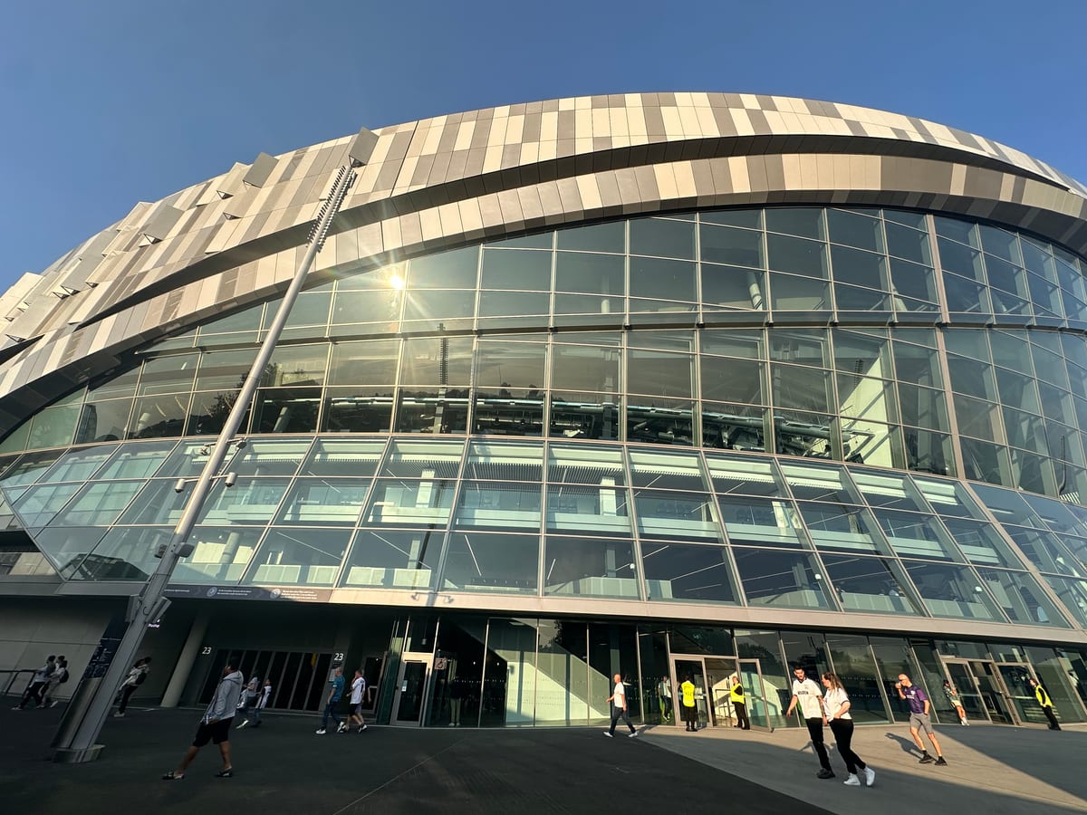 A curved glass-and-steel building photographed wide against the sky, distant figures at its base.