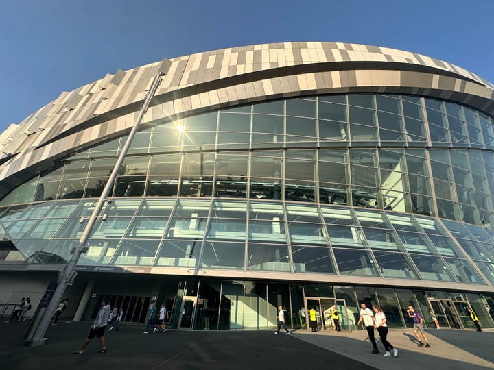 A curved glass-and-steel building photographed wide against the sky, distant figures at its base.
