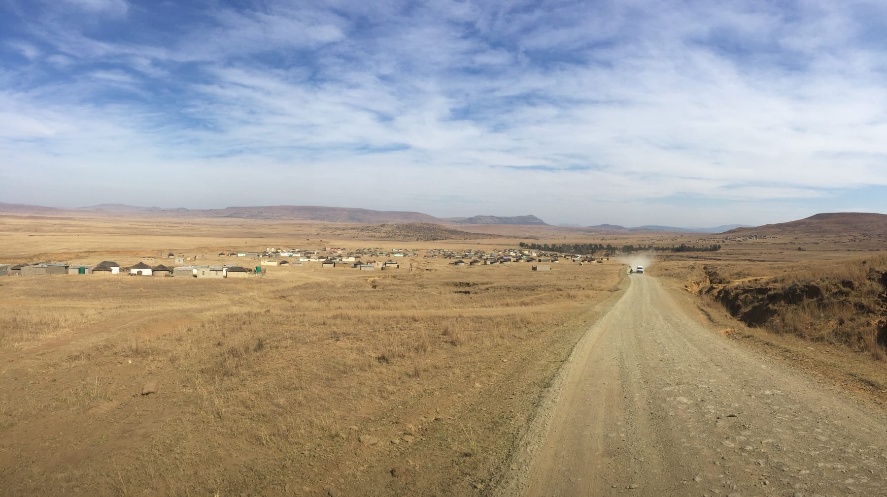 A dirt road running straight into a vast open plain beneath an enormous sky.