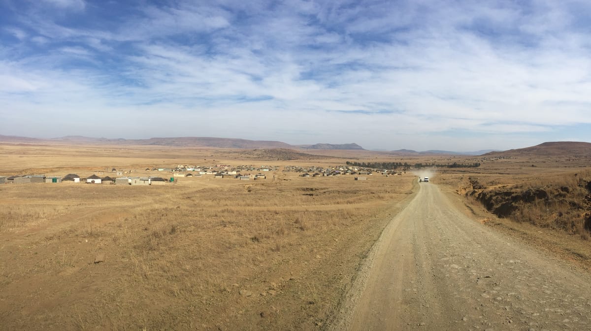 A dirt road running straight into a vast open plain beneath an enormous sky.