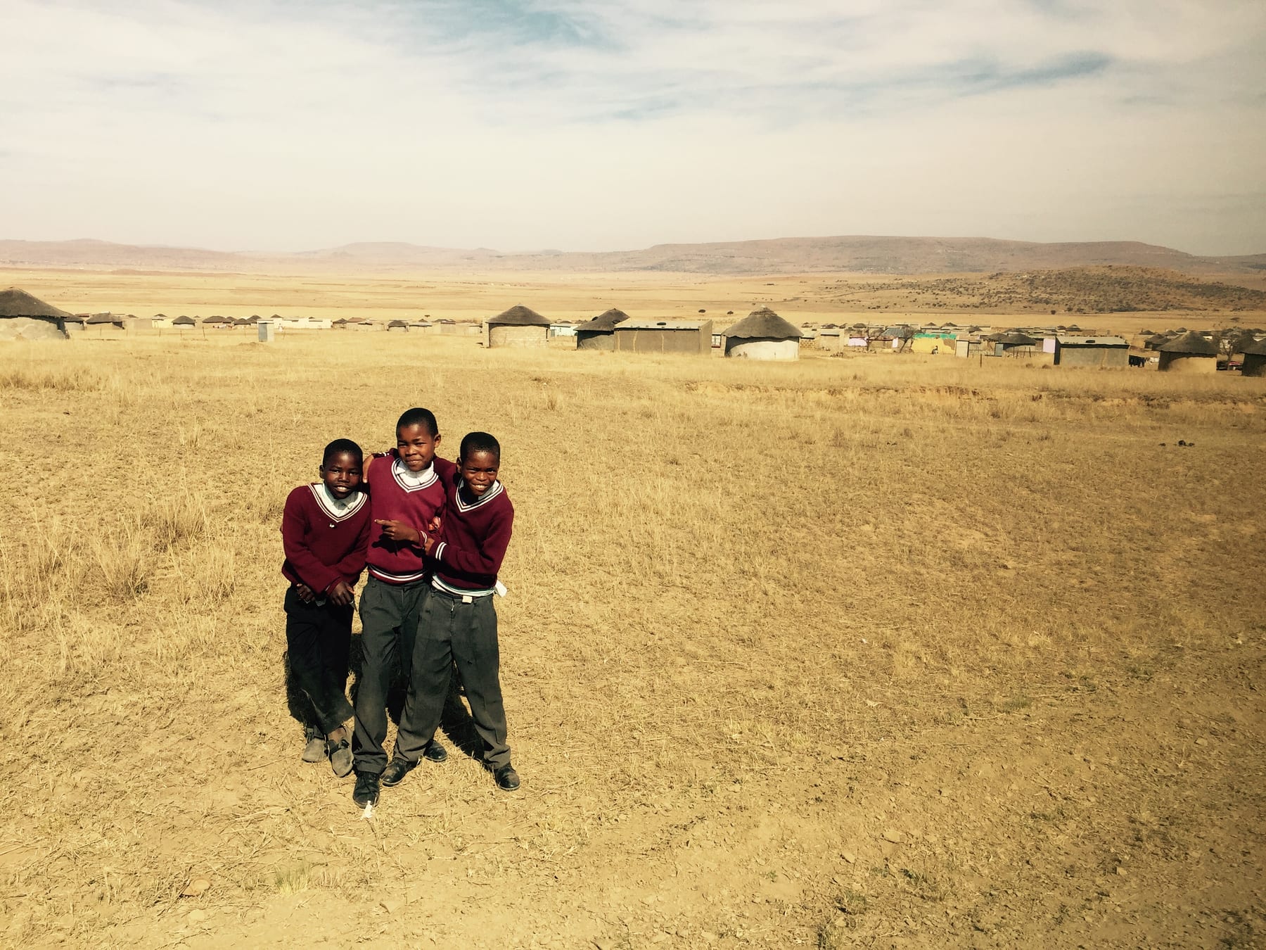 Two children in red school uniforms stand in open grassland.