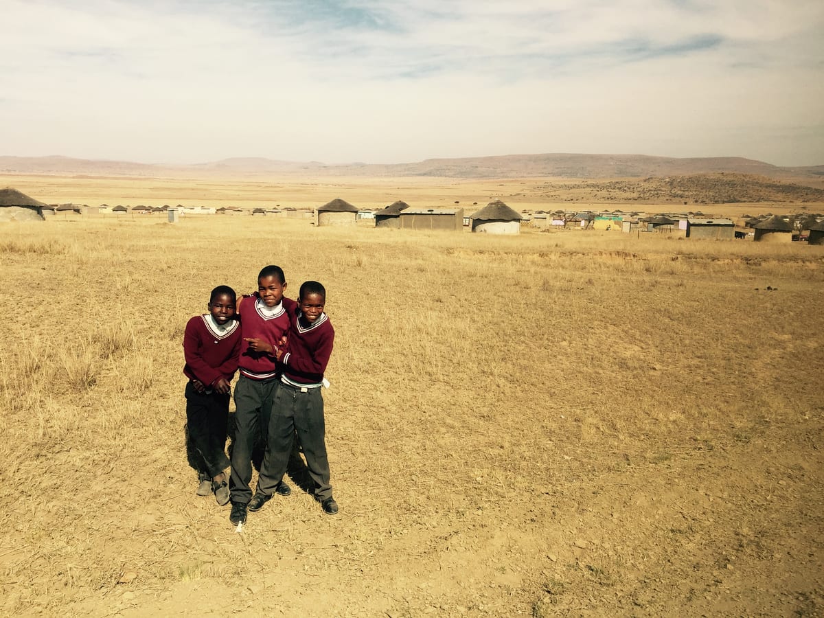Two children in red school uniforms stand in open grassland.