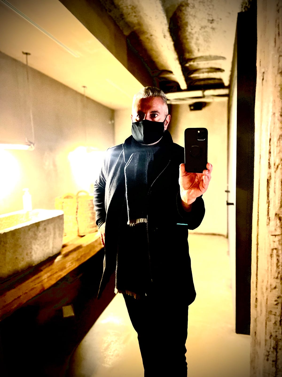A masked figure photographs themselves in a mirror along a warm-lit corridor.