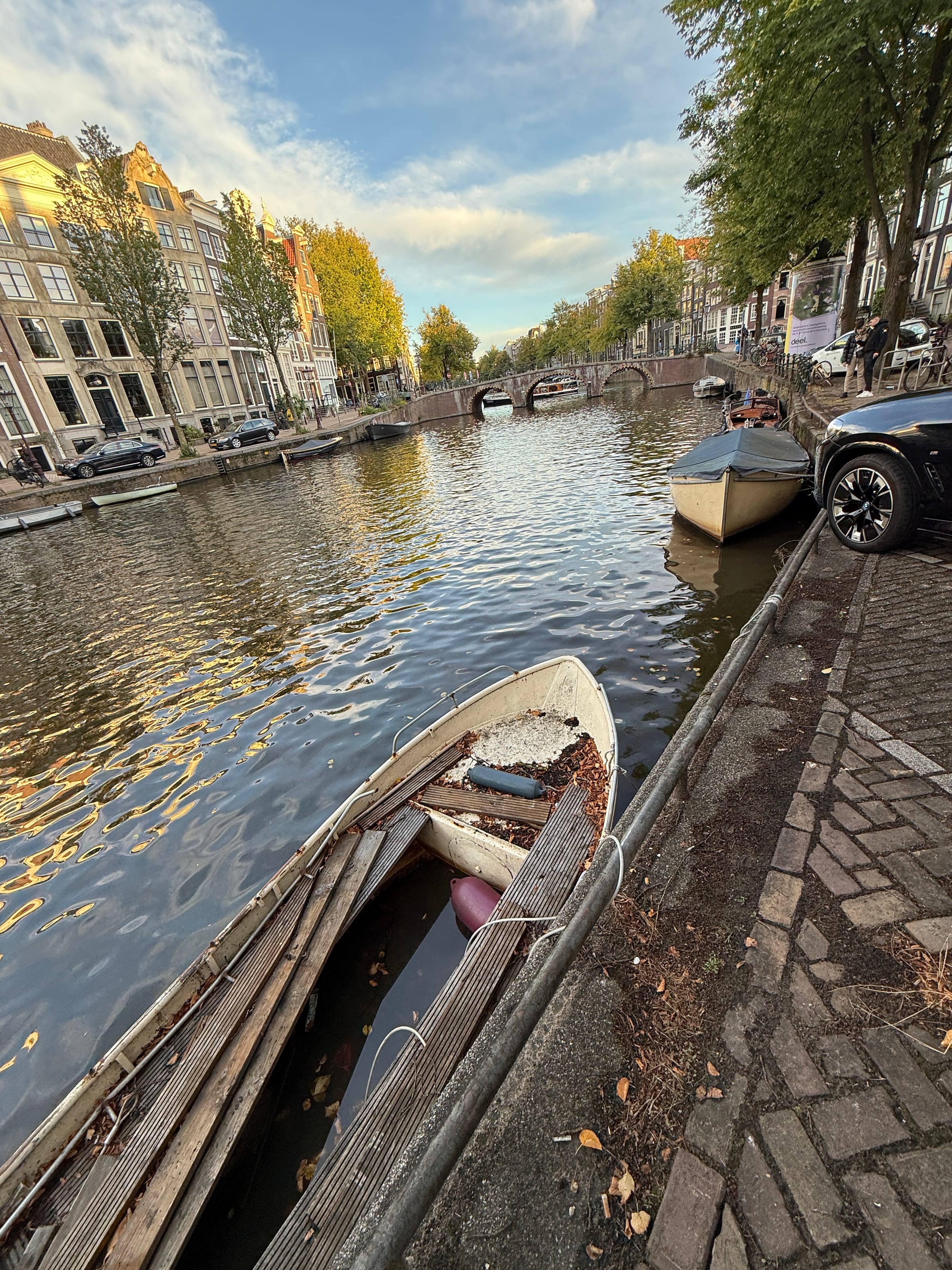 A small wooden boat moored on a still Amsterdam canal, bordered by autumn trees and water.