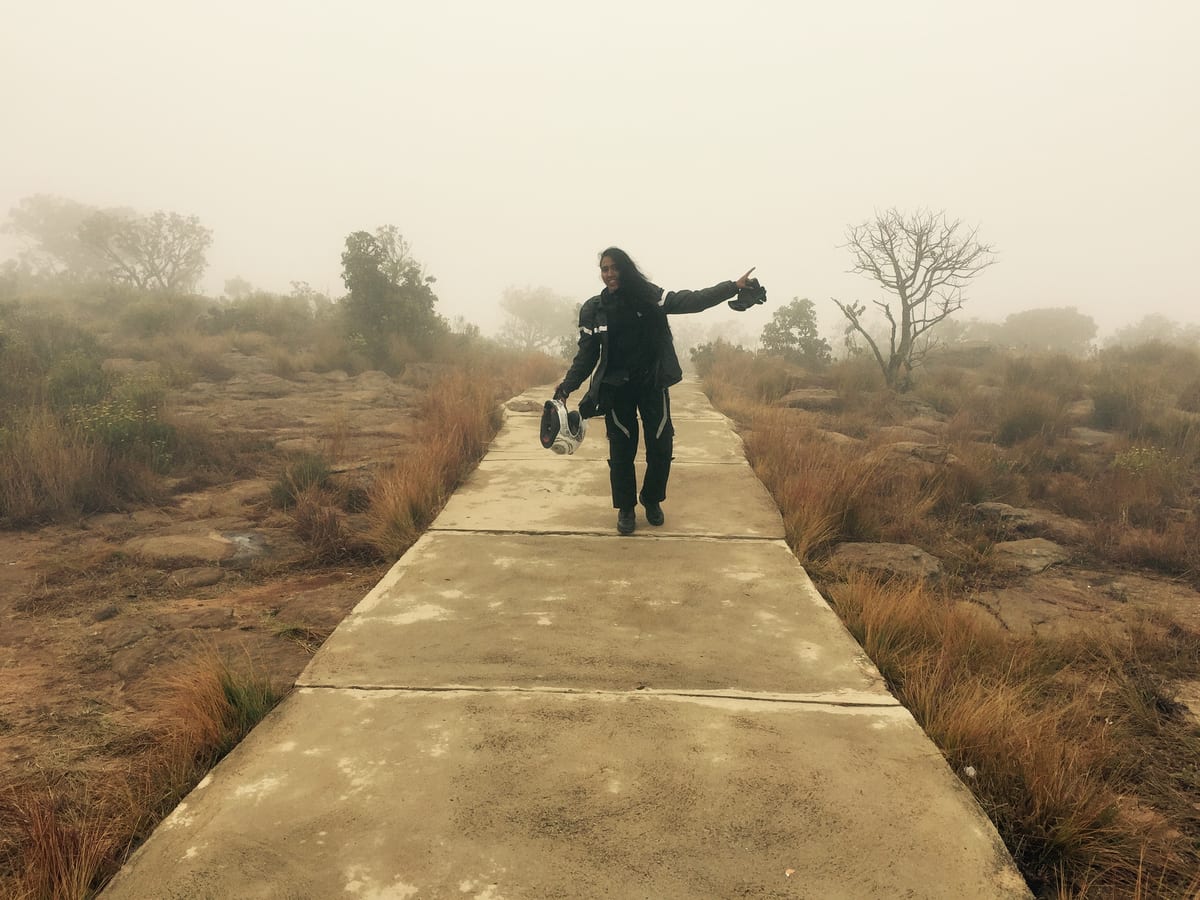 A distant figure stands on a long pathway in soft mist, arms loosely outstretched, far from the camera.