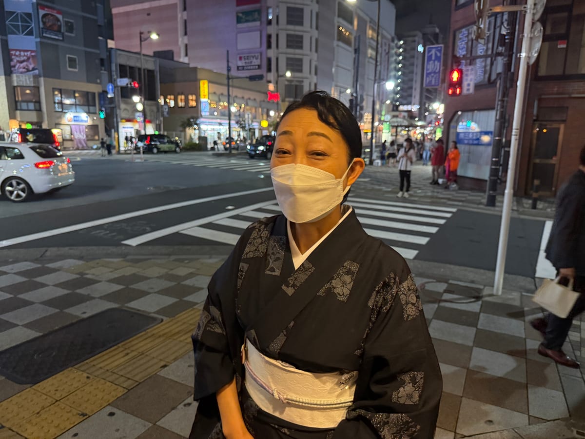 A woman in a patterned kimono waits at a neon-lit night crossing.
