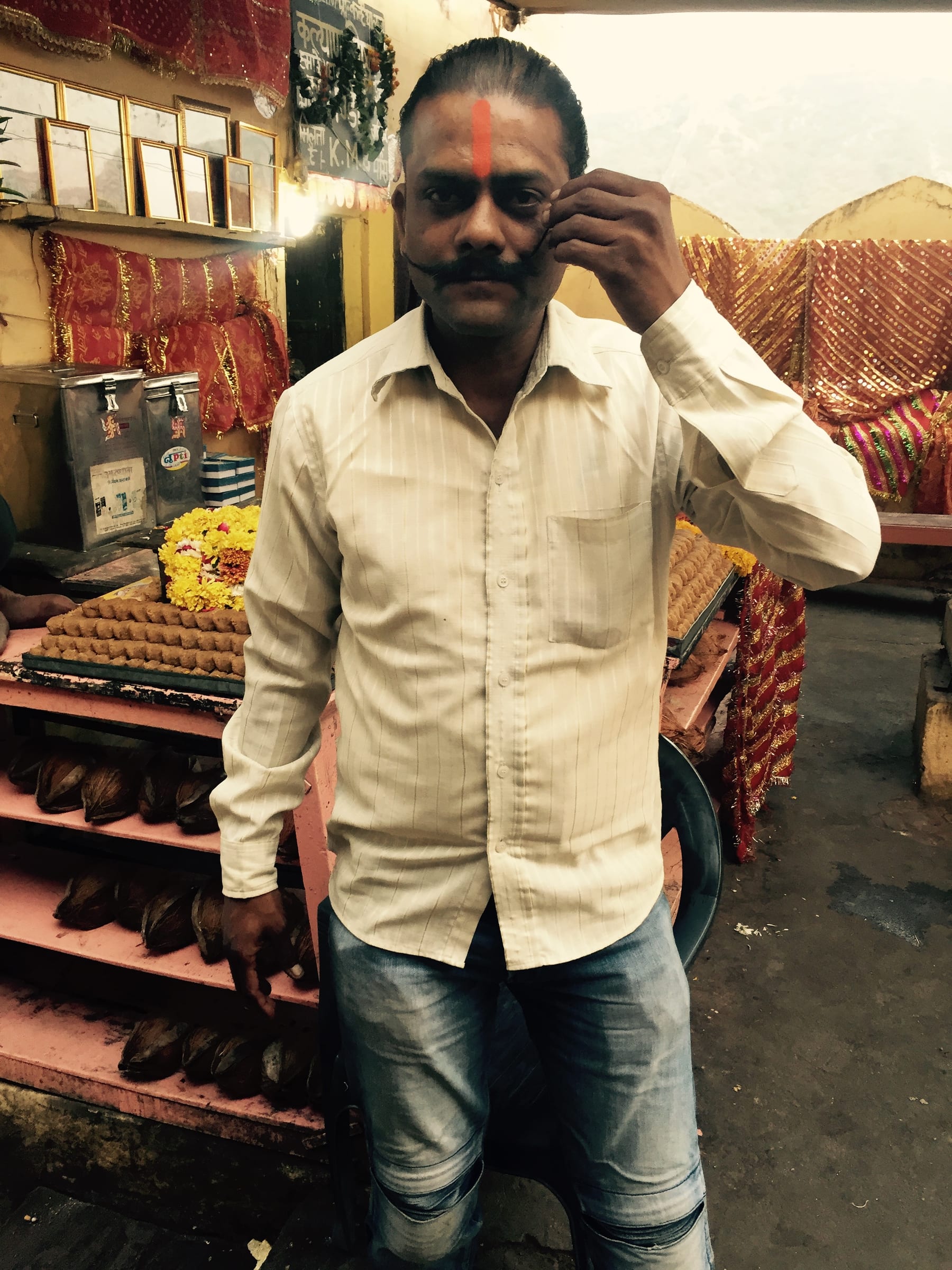 A man in a yellow shirt stands talking on a phone, market stalls behind him.