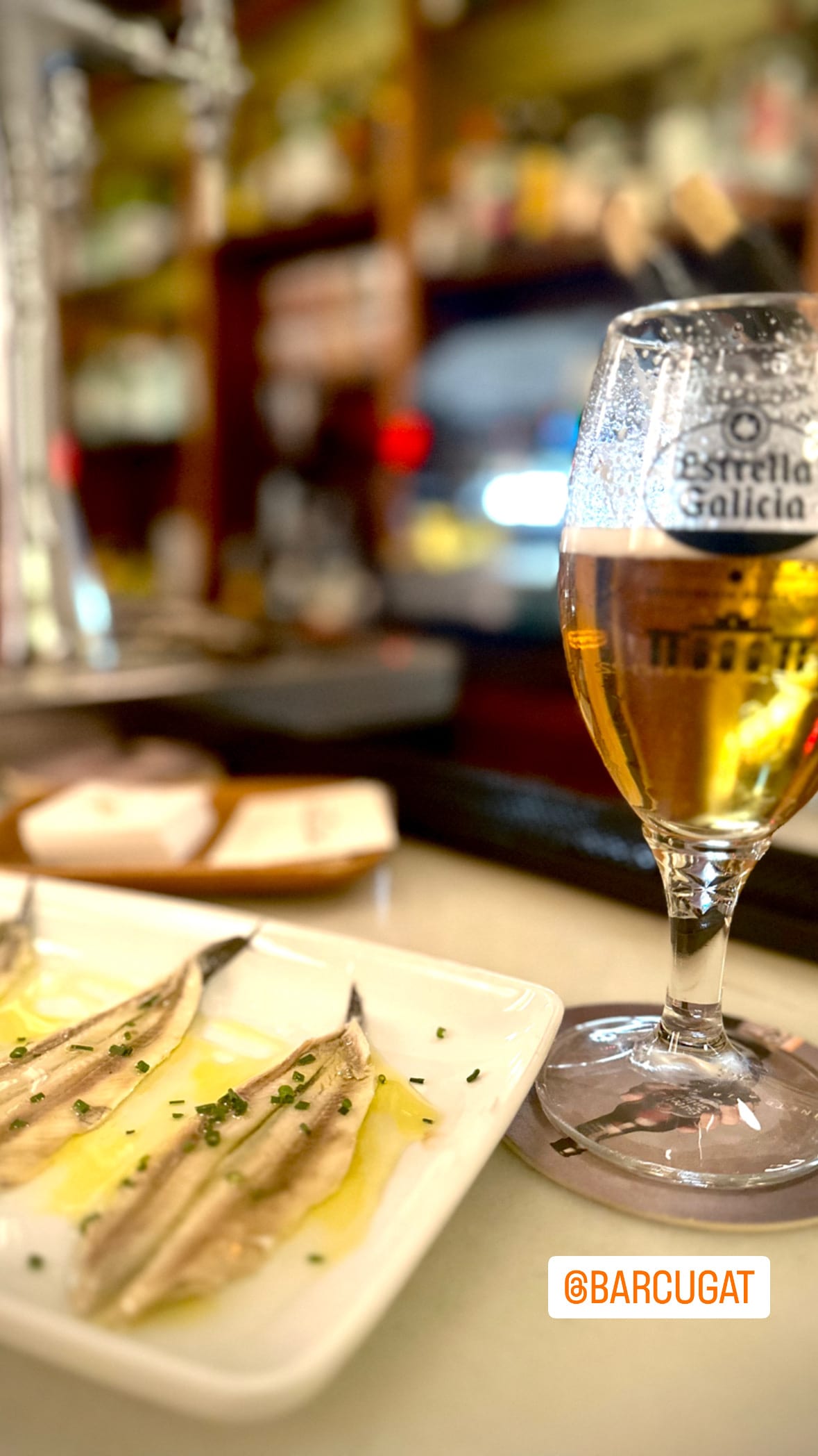 A glass of beer and a small plate of food on a table, close and warmly lit.