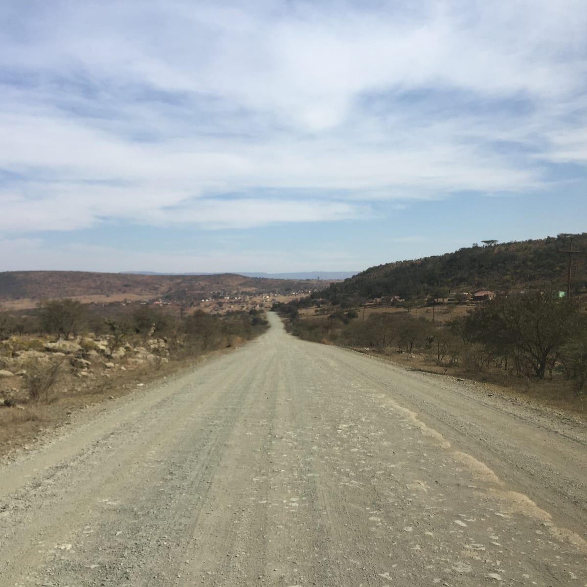 A gravel road running through bare hills under hazy light, the way ahead empty.
