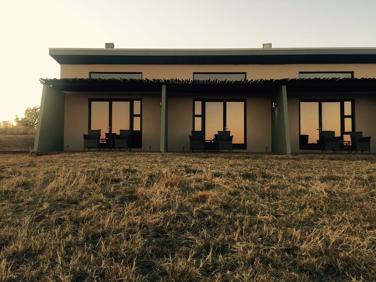 A low modern lodge with lit windows at dusk, set against open country and a fading sky.