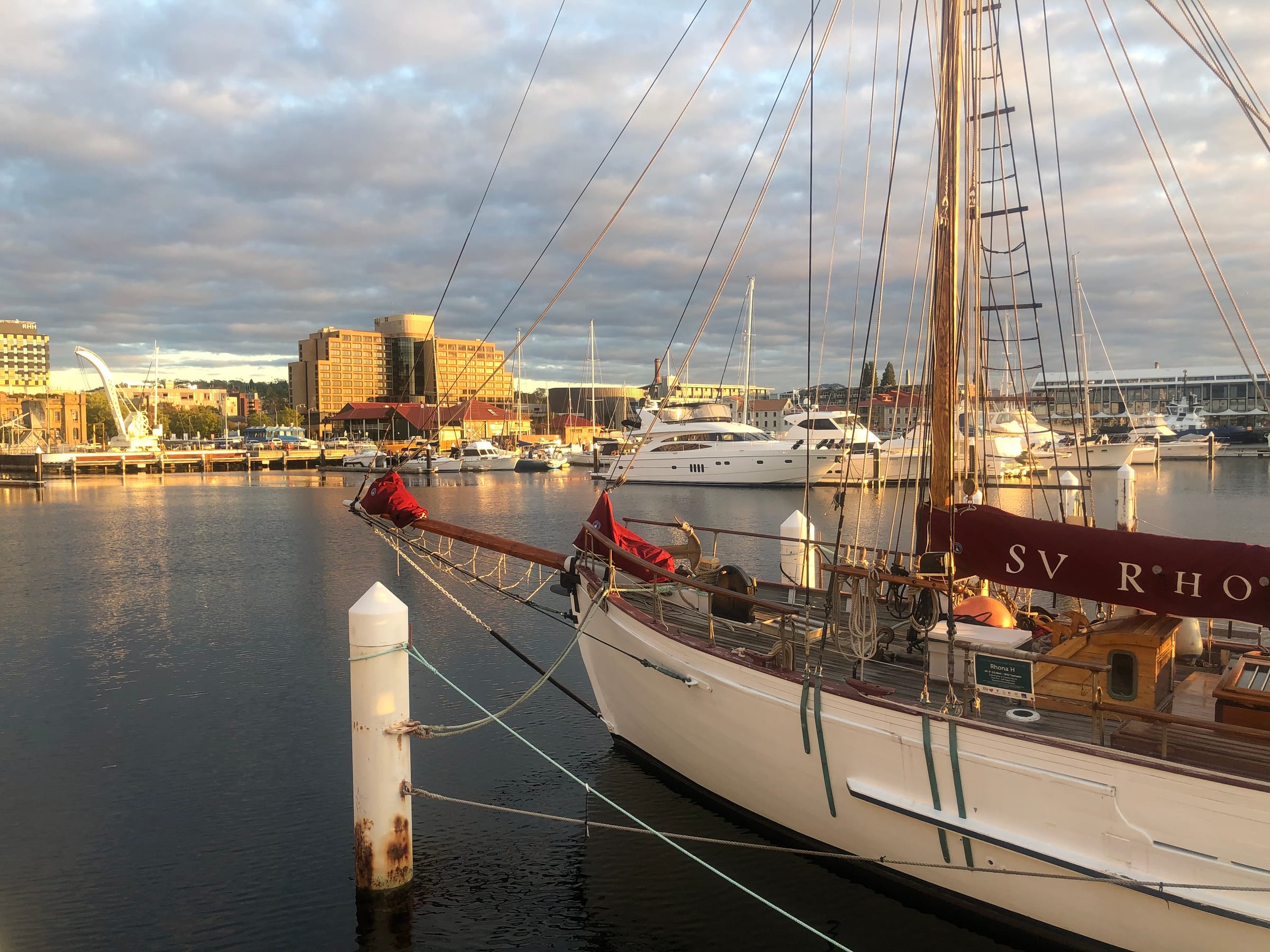 Tall sailing-ship masts rising over a quiet harbour, a low town behind.