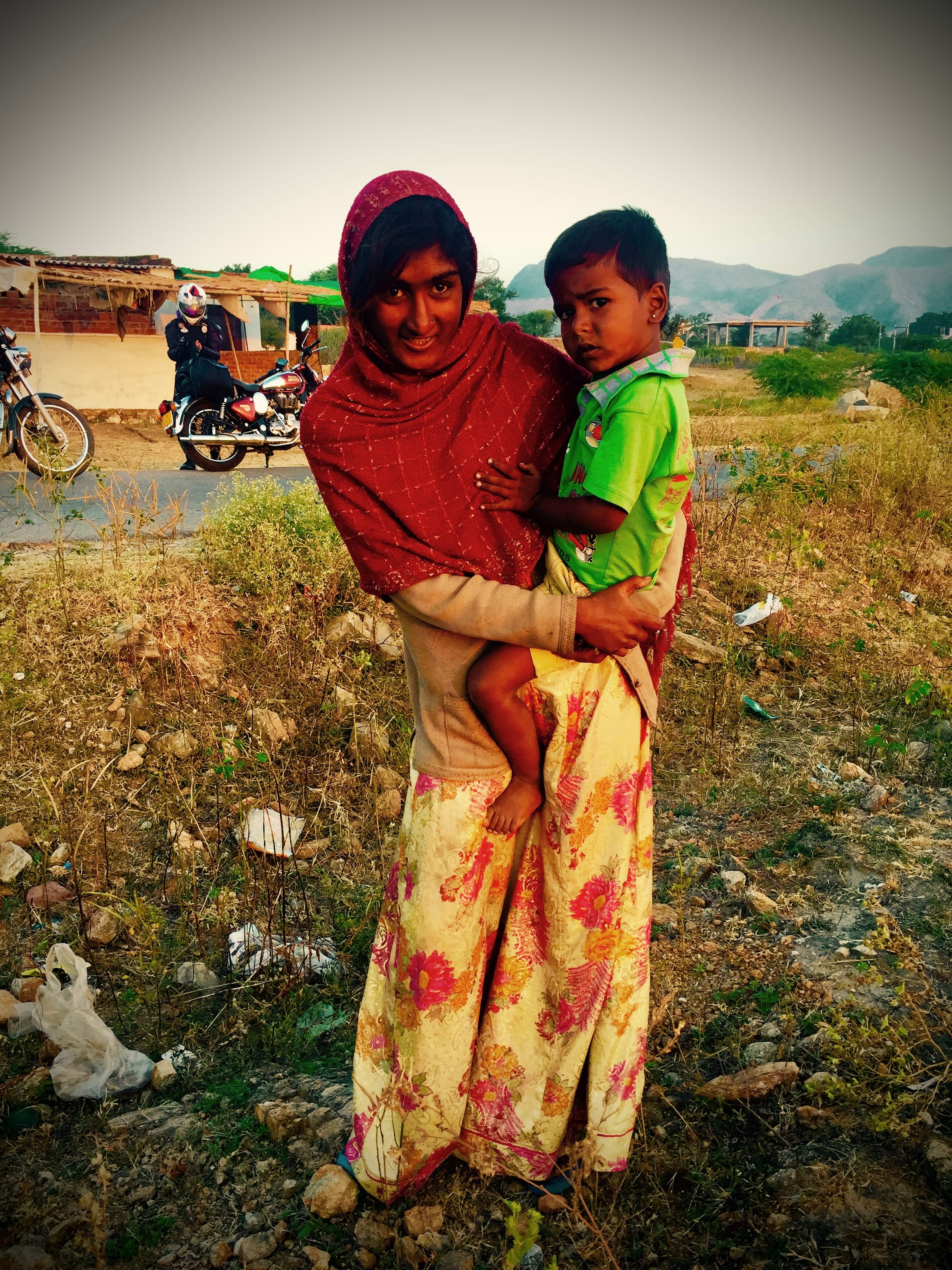 A woman holds a small child in an open field.