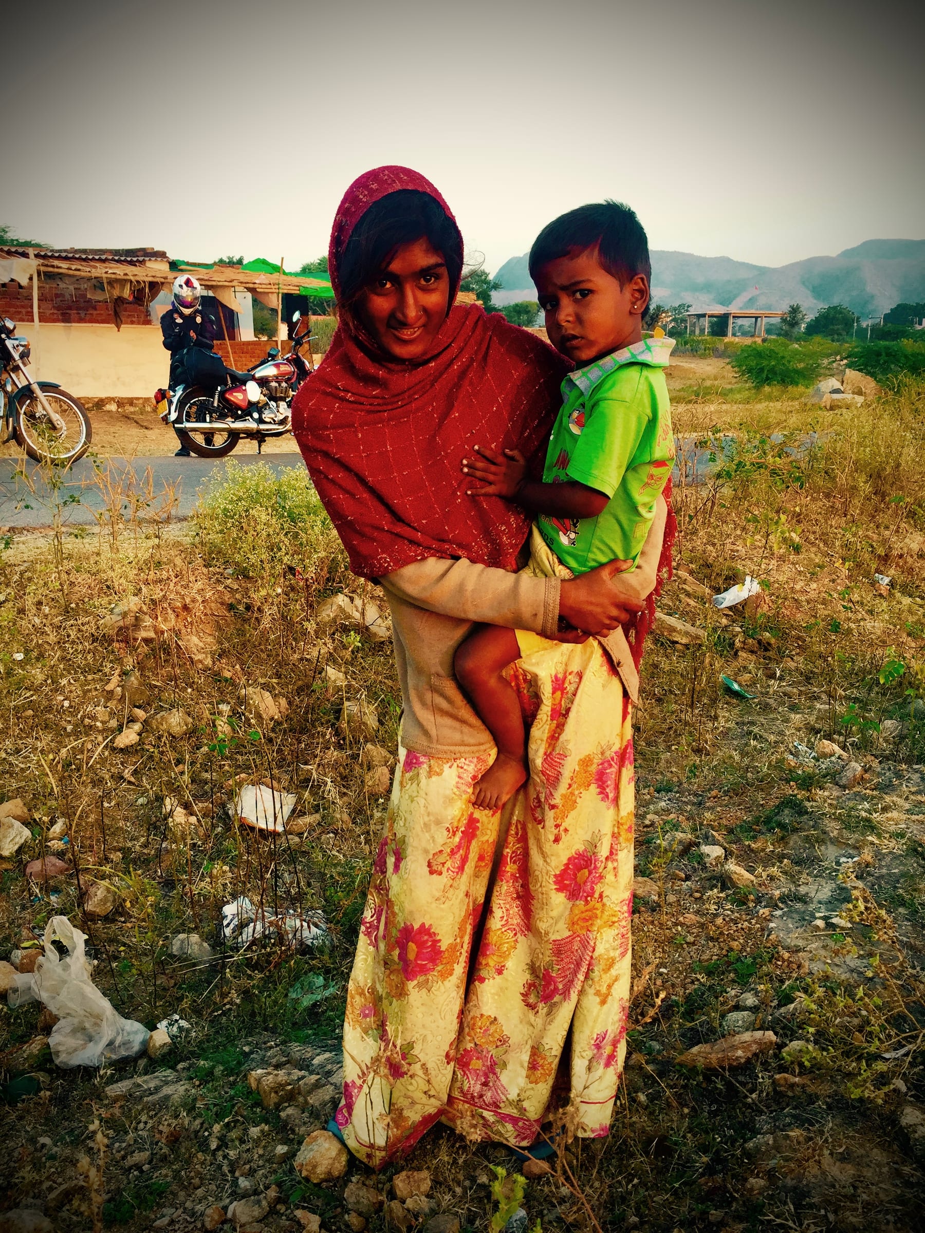 A woman holds a small child in an open field.