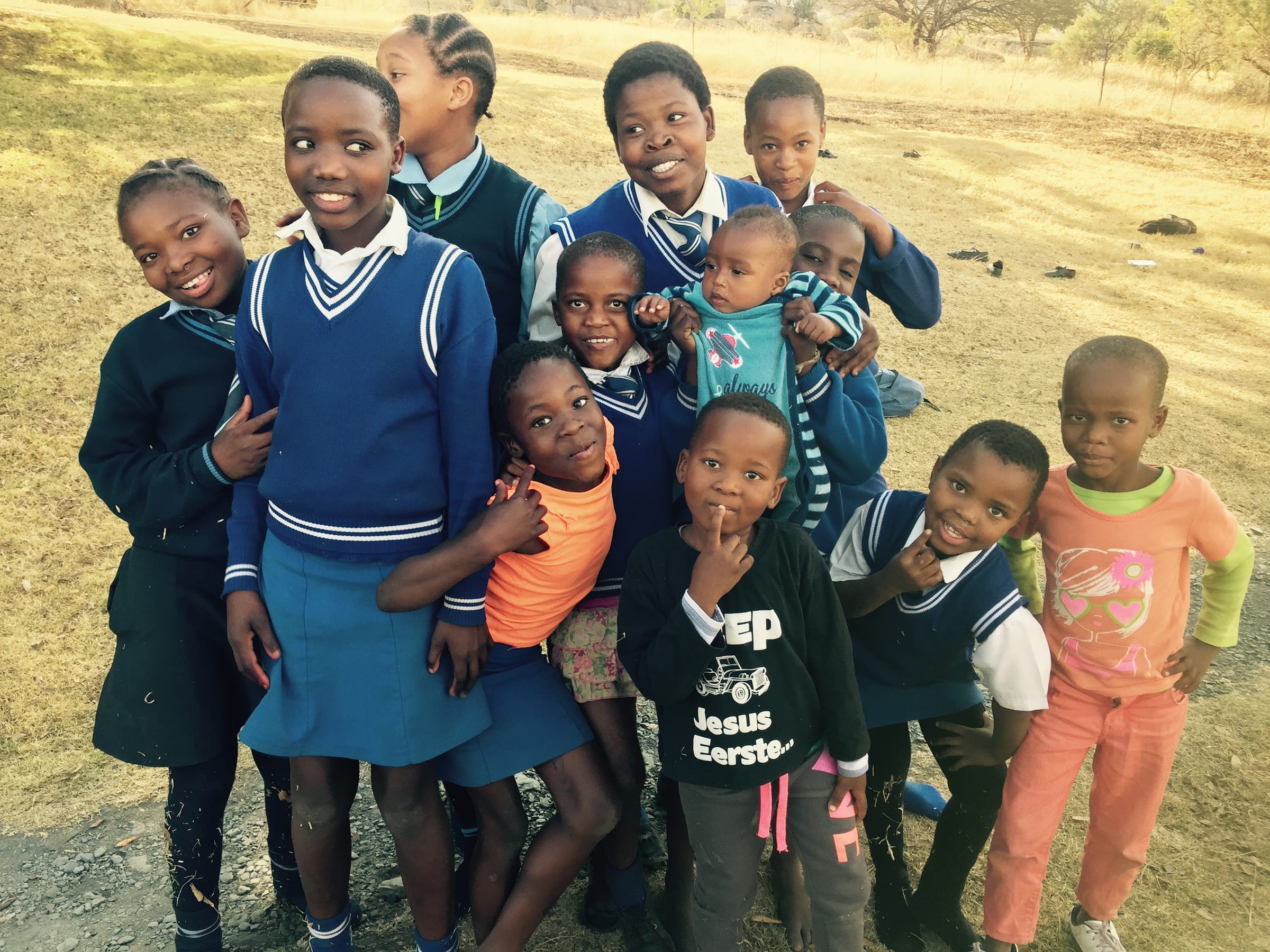 A group of school children gather together in a rural landscape.