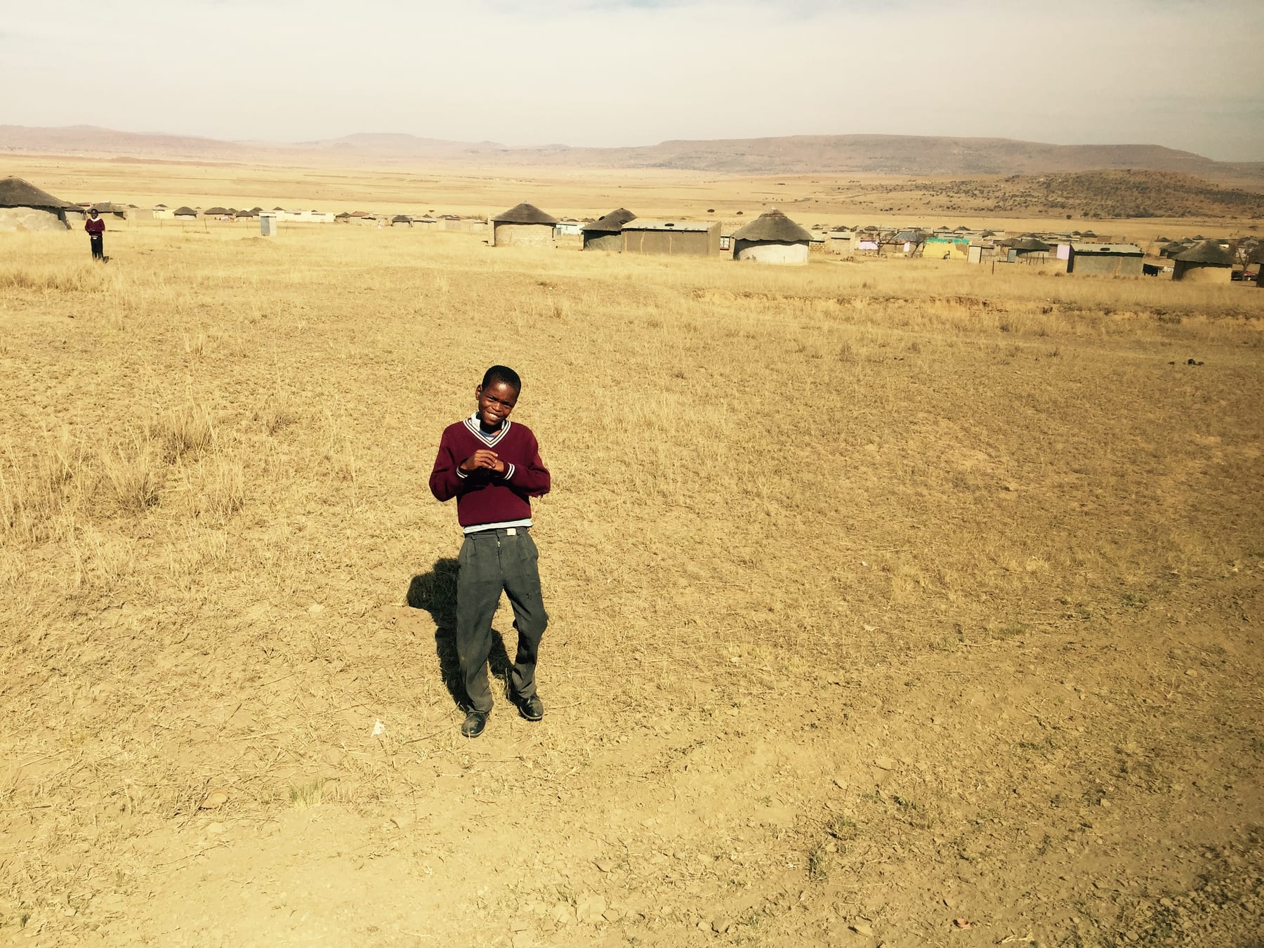 A figure in red sits on a grassy hillside above an open valley.