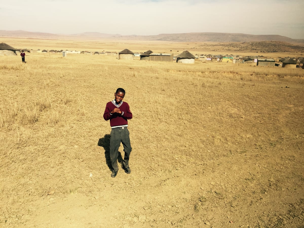 A figure in red sits on a grassy hillside above an open valley.