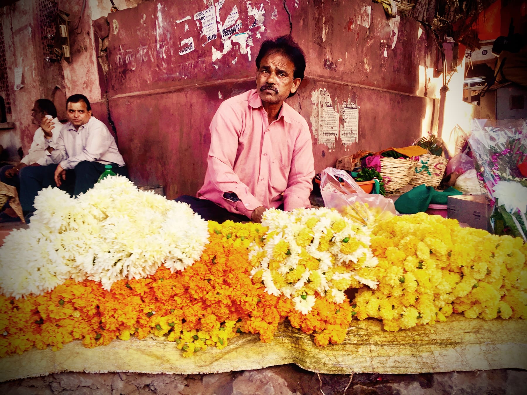 A market stall heaped with bright marigold garlands in orange and yellow, a vendor working behind the flowers.