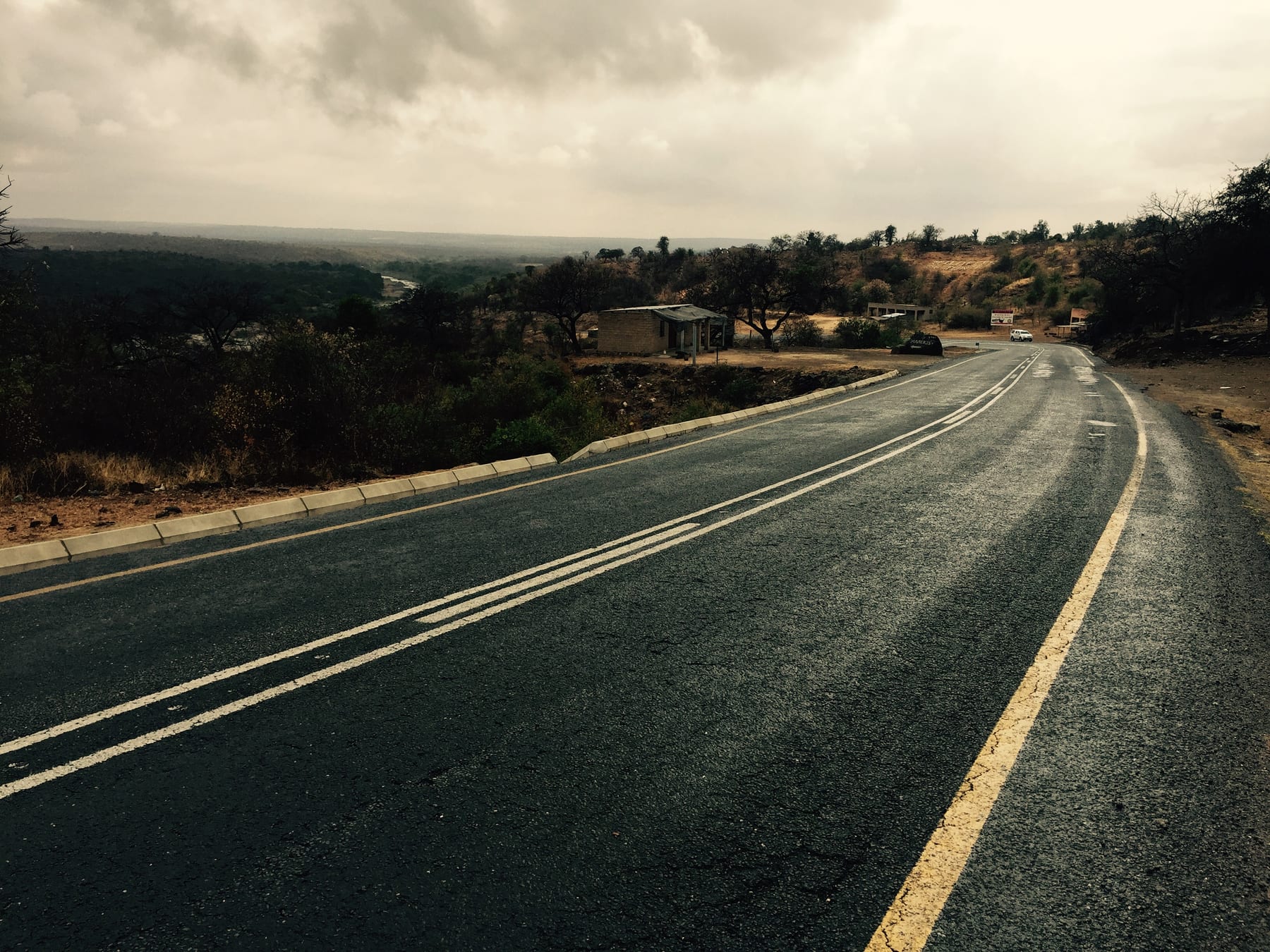 An empty tar road curving over a rise into open grassland under a grey, weather-heavy sky.