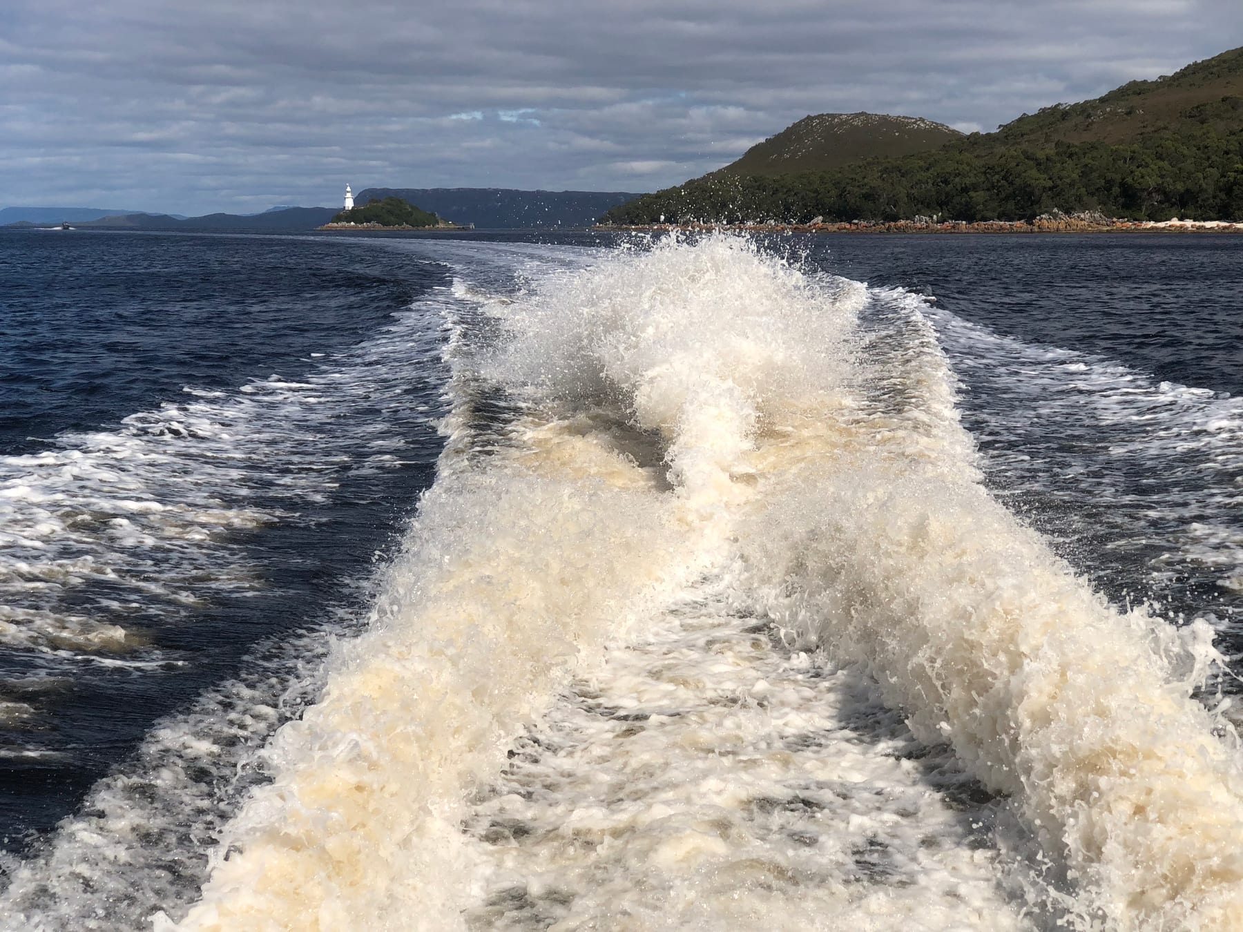 The churning white wake of a boat spreading across deep blue water.