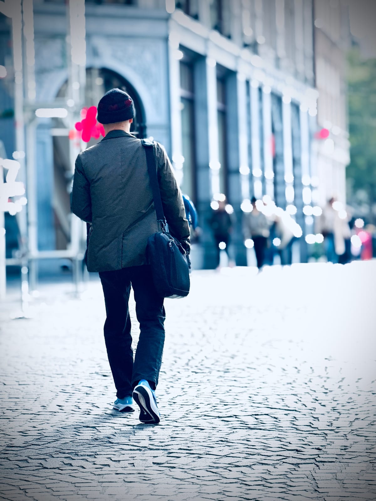 A lone figure with a backpack walks away down a pale stone street, seen from behind.