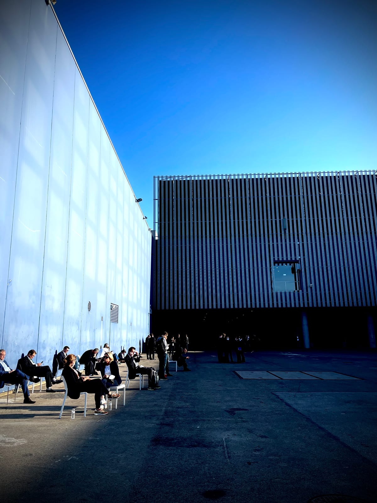 A white modernist museum building against a deep blue sky, small distant figures on the open plaza.