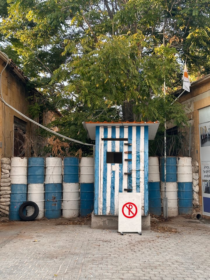 Blue and white painted oil drums standing under a tree beside a rough wall, a discarded tyre nearby.