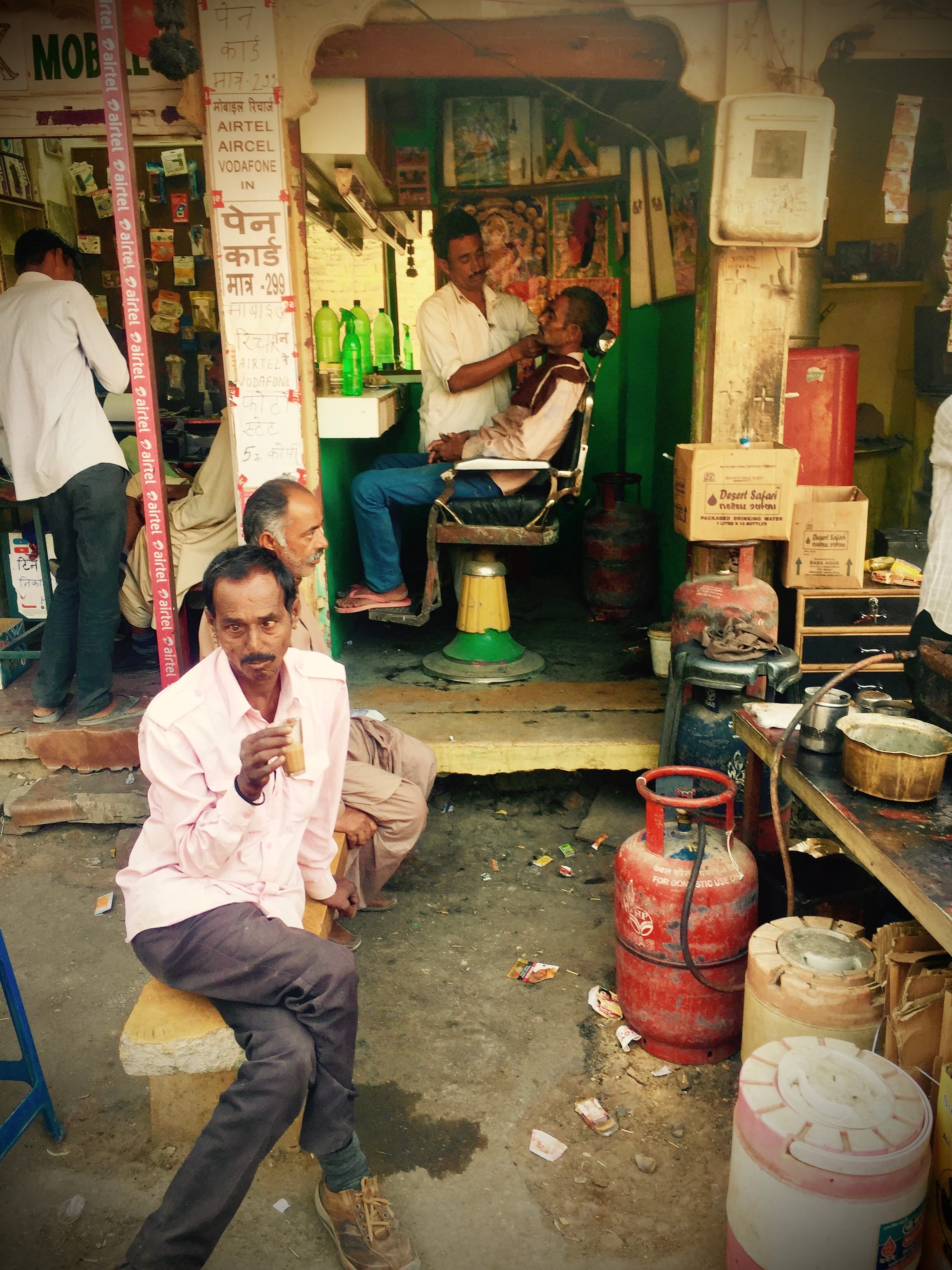 A man sits at the front of a small roadside shop.