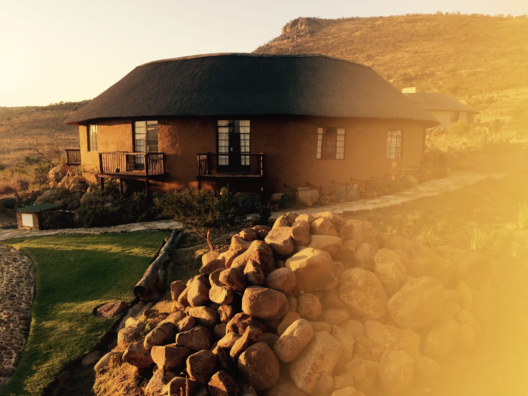 A round thatched hut catching warm golden-hour light against dry grass and soft sky.
