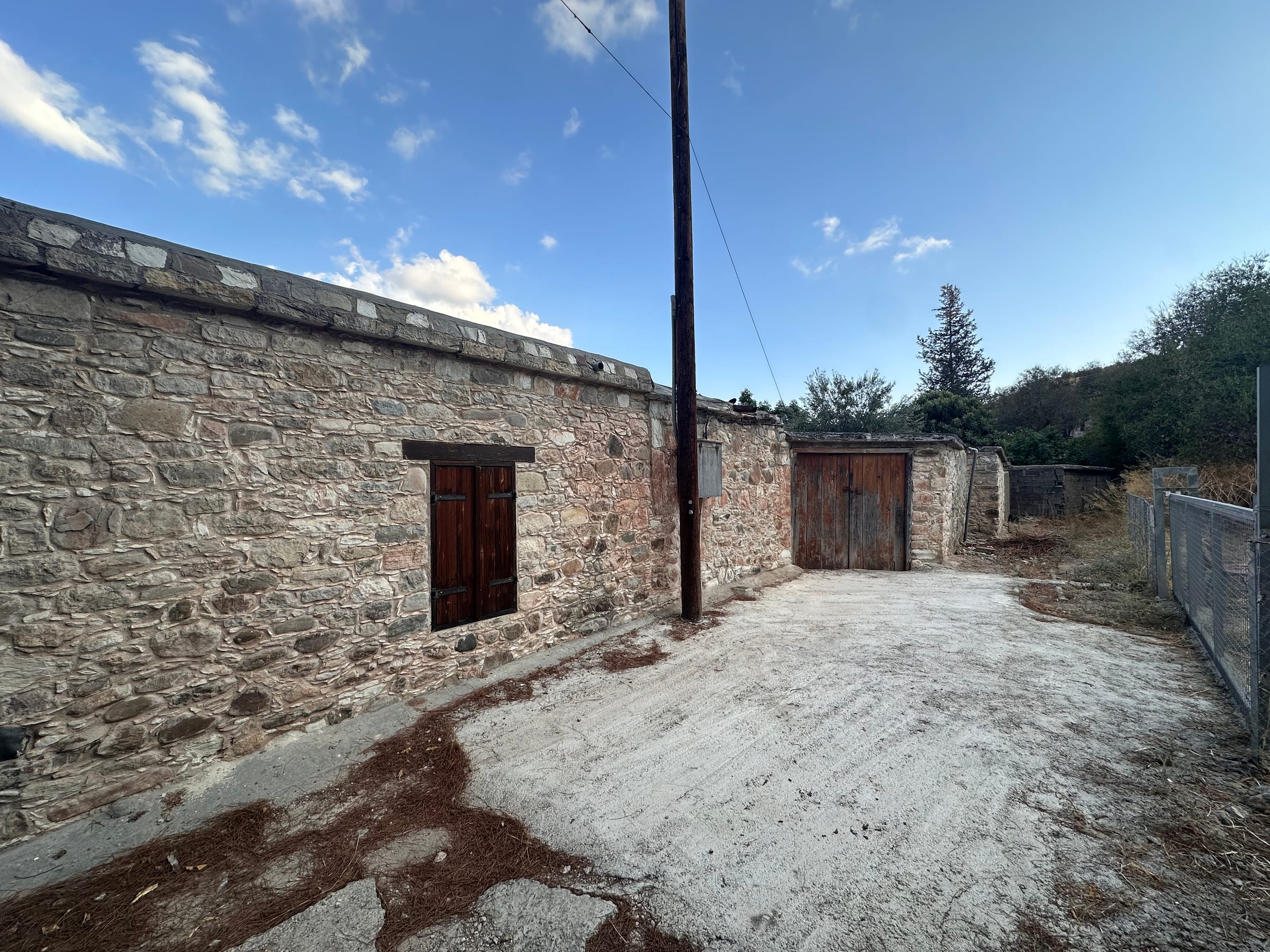 A weathered stone building beside a bare dirt yard, a power pole rising against blue sky.