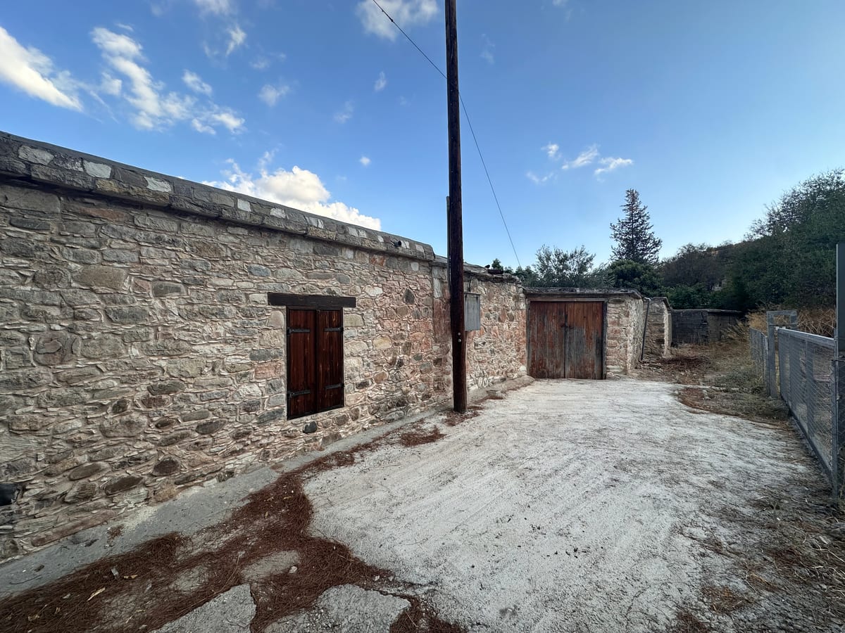 A weathered stone building beside a bare dirt yard, a power pole rising against blue sky.