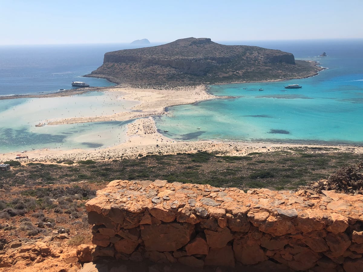 A turquoise lagoon curving between pale sandbars and rocky headlands, seen from a height.