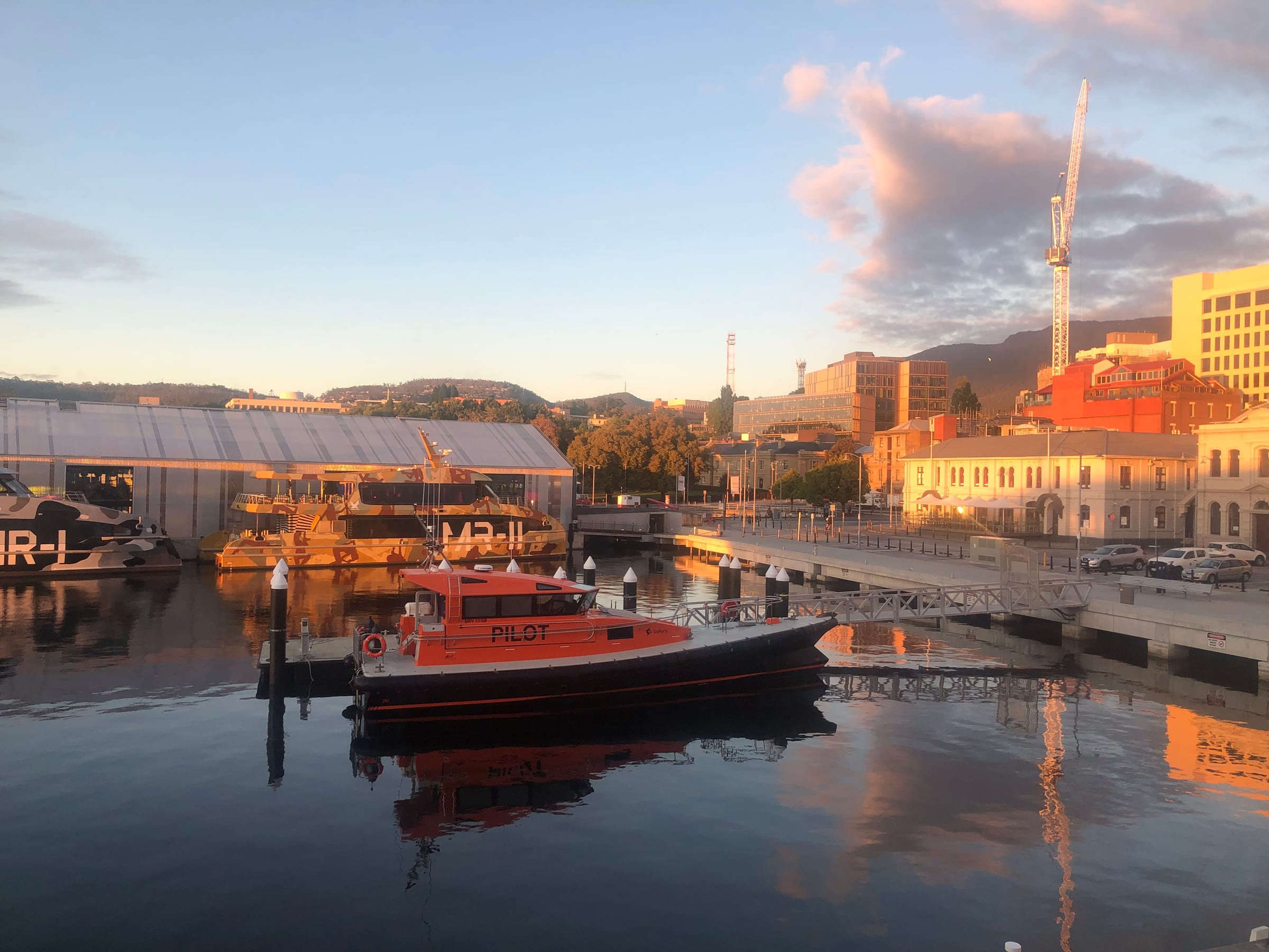 A harbour at dusk, moored boats and waterfront buildings mirrored in still water.