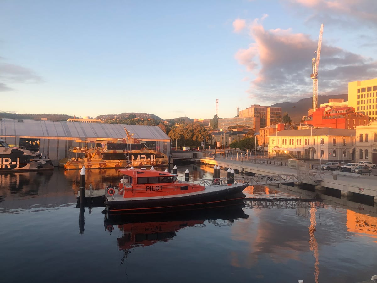 A harbour at dusk, moored boats and waterfront buildings mirrored in still water.
