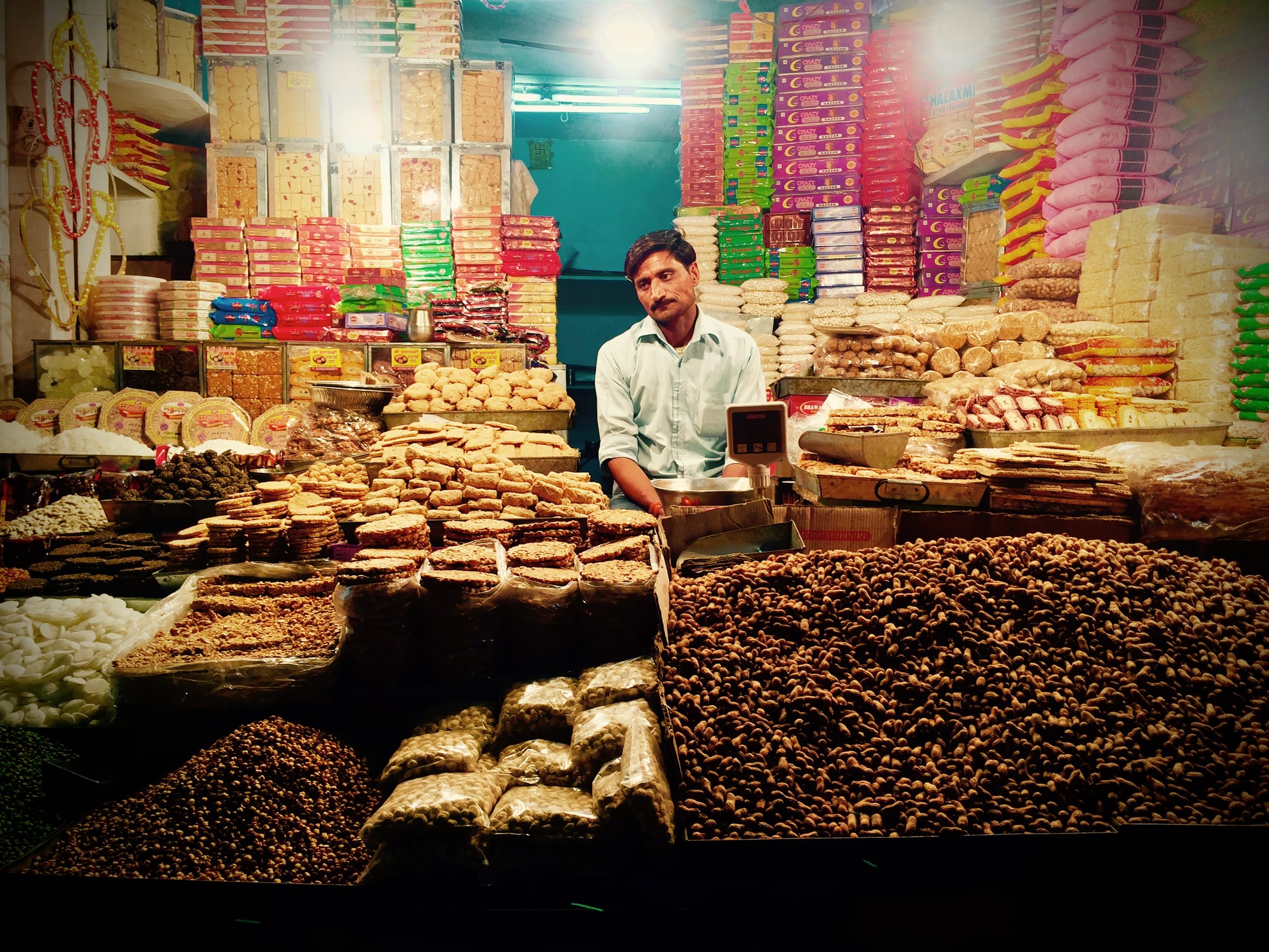 A market stall laid with trays of sweets, a vendor standing behind.
