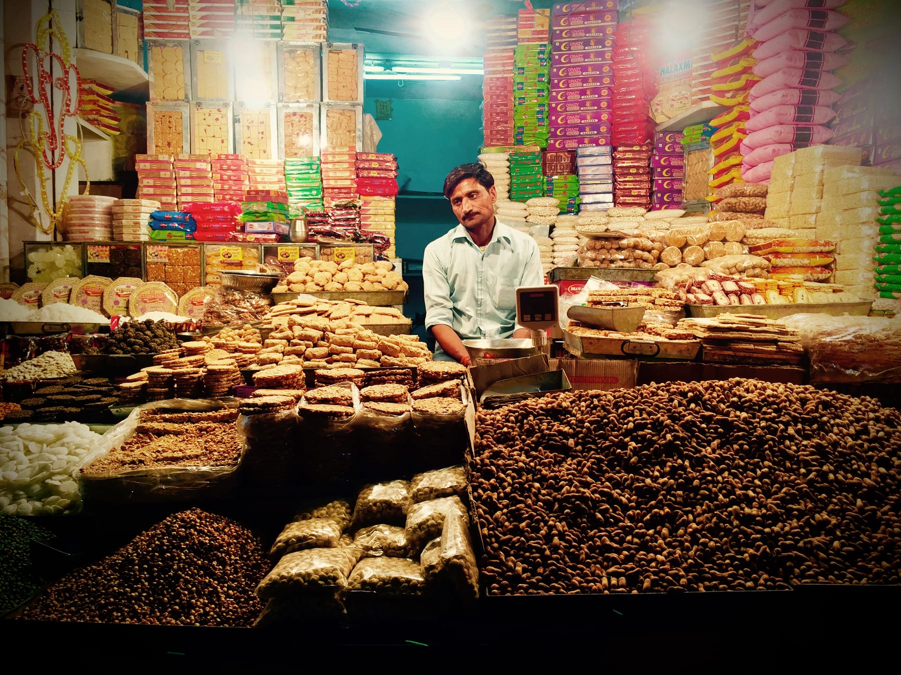 A market stall laid with trays of sweets, a vendor standing behind.