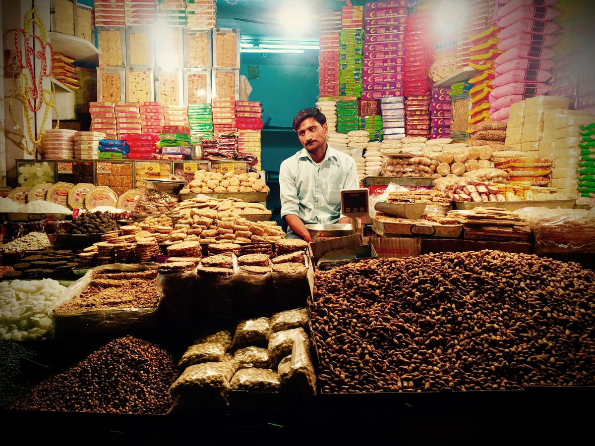 A market stall laid with trays of sweets, a vendor standing behind.